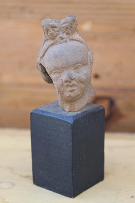 Lot 1767 - Ancient Greek terracotta head fragment, 6cm high, raised on a hardwood and marble stand, together with a similar fragment and one other (3)