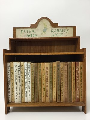 Lot 557 - Collection of twenty-one Beatrix Potter Peter Rabbit books contained in a wooden bookshelf, 37cm high overall