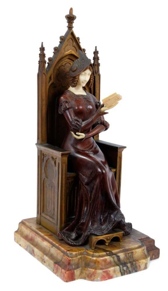 Lot 823 - In the manner of Jean Dampt (1854 - 1945): a late 19th century French Gothic Revival bronze, ivory and rosewood figure of a young woman dressed in medieval costume, seated on a throne reading a boo...