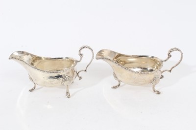 Lot 313 - Pair of late Victorian silver sauce boats of helmet form, with scroll handles, gadrooned borders and engraved armorials, each raised on three hoof feet, (London 1900), maker William Hutton & Sons L...