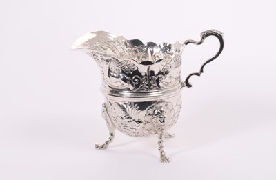 Lot 314 - Edwardian silver milk / cream jug of helmet form with chased and embossed decoration depicting flowers and animals, with scroll handle, raised on three hoof feet, (Chester 1902), maker George Natha...