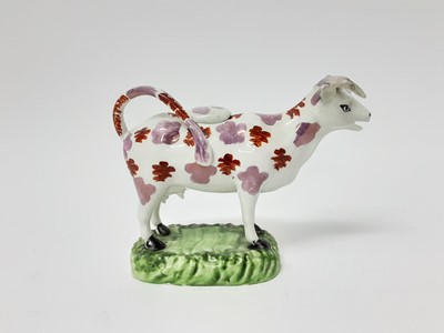 Lot 184 - Early 19th century Swansea type pottery cow creamer and cover, painted in purple lustre and red enamel on a green base, 18cm long