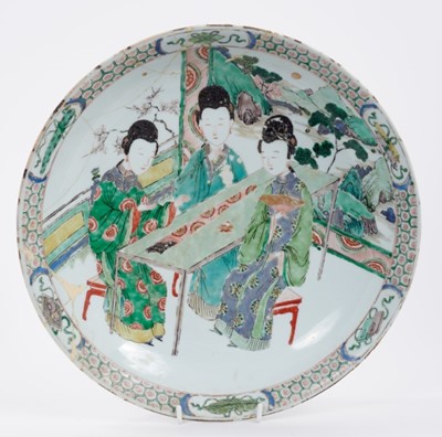 Lot 189 - Chinese famille verte dish, Kangxi period, decorated with three female figures seated on stools by a table, landscape in the background, the edge with panels containing auspicious symbols on a diap...