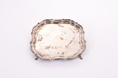 Lot 346 - George V silver card salver of square form, with piecrust borders, raised on four hoof feet, (Chester 1912) maker W.E.B.F.E.B., all at approximately 16oz, 21cm in diameter