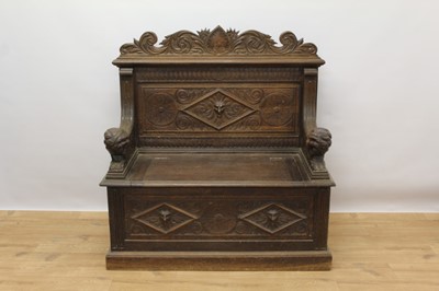 Lot 1453 - Victorian carved oak bench, with panel back centred by carved mask and box base with hinged seat, flanking carved lion arms, 100cm wide