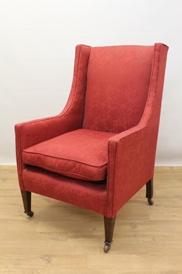 Lot 1353 - Edwardian wing armchair upholstered in red fabric, on mahogany square taper legs terminating on brass and ceramic castors