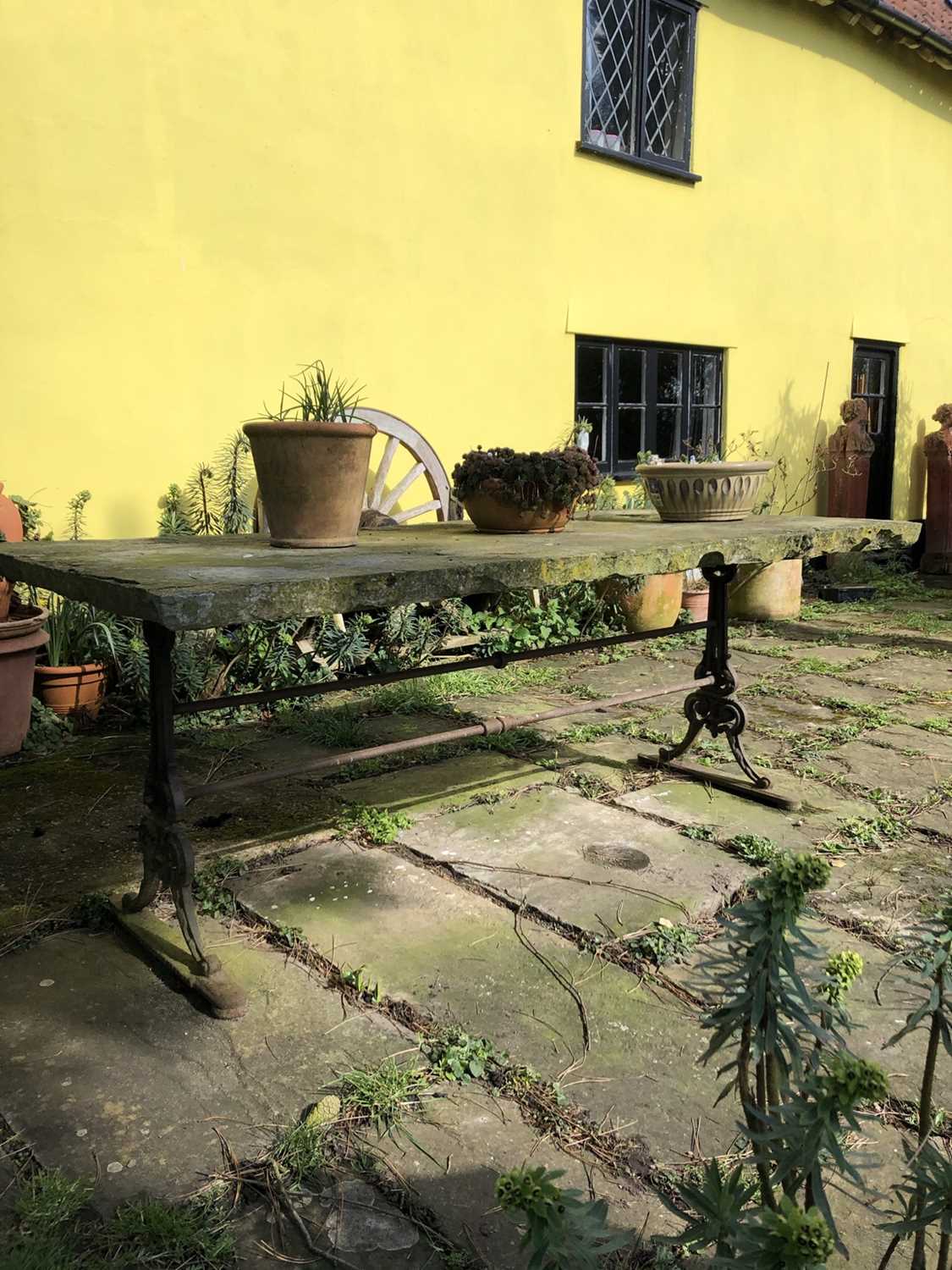 Lot 1865 - Massive garden table with rectangular York stone top, supported on a cast iron base with shaped standard ends, 205cm long x 100cm wide