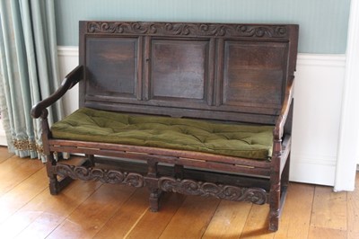 Lot 1375 - Late 17th/early 18th century oak settle, the top rail carved with scrolling foliate decoration over a triple panelled back and downswept arms, the buttoned cushioned seat supported by ropes, in tur...