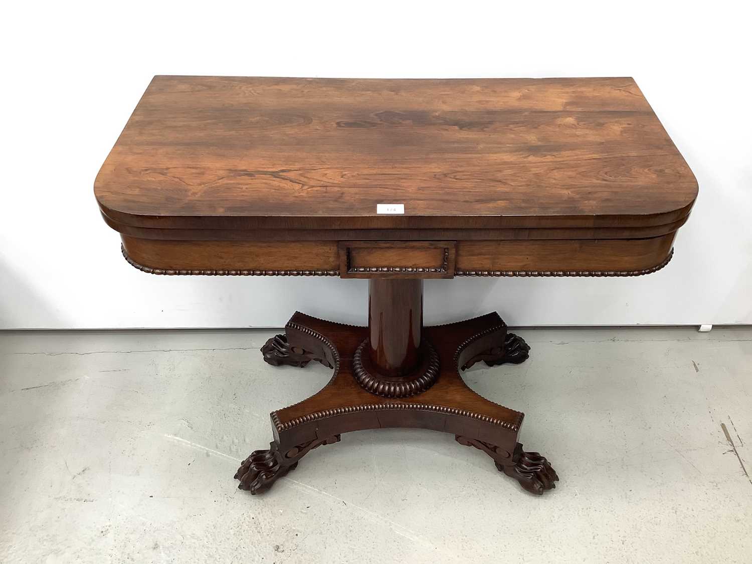 Lot 174 - 19th century rosewood card table with foldover revolving top on turned column and quatrefoil base with carved paw feet, 90.5cm wide x 14.5cm high