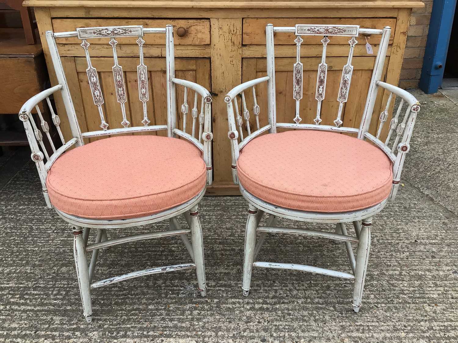 Lot 919 - Pair of painted open elbow chairs with decorative shaped backs, caned seats with cushions, on shaped legs joined by stretchers