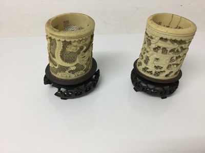Lot 381 - Two Chinese Canton reticulated ivory brush pots on wooden stands, one carved with figures, the other with dragons, 12cm high