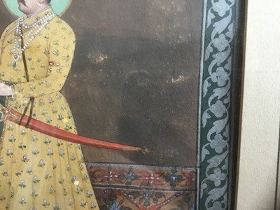 Lot 765 - Indian painting of a Jaipur nobleman In yellow embroidered robes, holding a rose, standing on a carpet, within ornamental painted border, framed and glazed, late Mughal school, probably Rajahstan c...