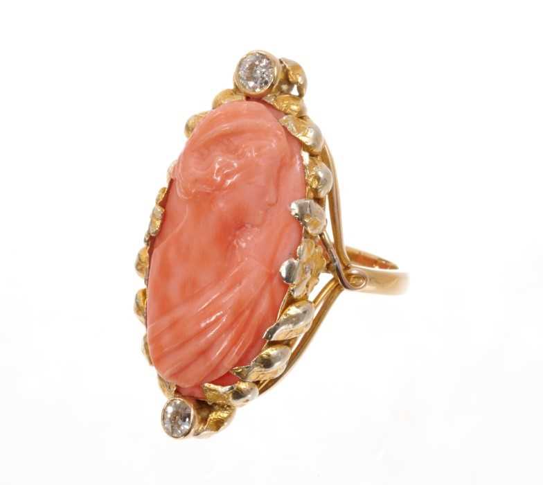 Lot 1976 - Carved coral cameo and diamond ring with an oval relief carved coral cameo depicting a classical female profile bust, flanked by two old cut diamonds in gold setting with applied foliage on plain s...