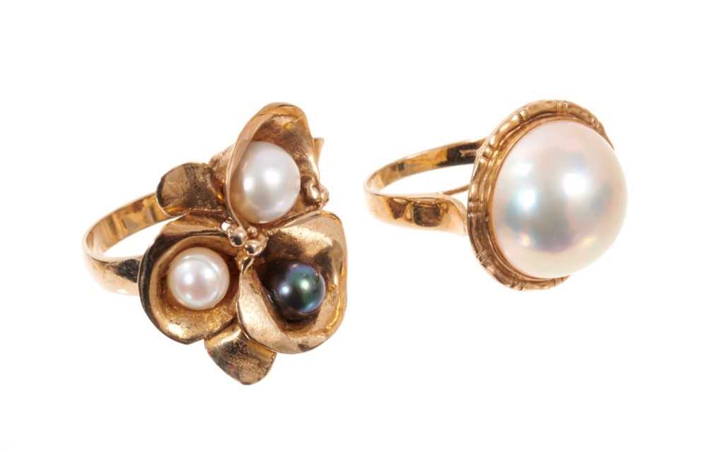 Lot 1981 - Two gold and cultured pearl dress rings, one with black, grey and white cultured pearls in 9ct gold setting (London 1988), the other with a cultured Mabe pearl measuring approximately 15mm in 9ct g...