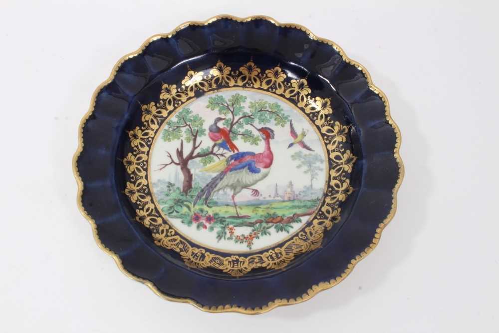Lot 13 - Worcester plate, circa 1770, of fluted form, polychrome painted with exotic birds, on a cobalt blue and gilt-patterned ground, seal mark to base, 19cm diameter