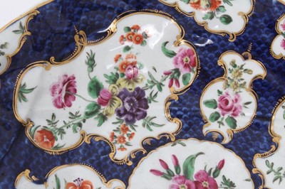 Lot 70 - Worcester cabbage leaf dish, circa 1770, painted with panels of flowers with gilt scrollwork borders, on a blue scale ground, seal mark to base, 26cm long