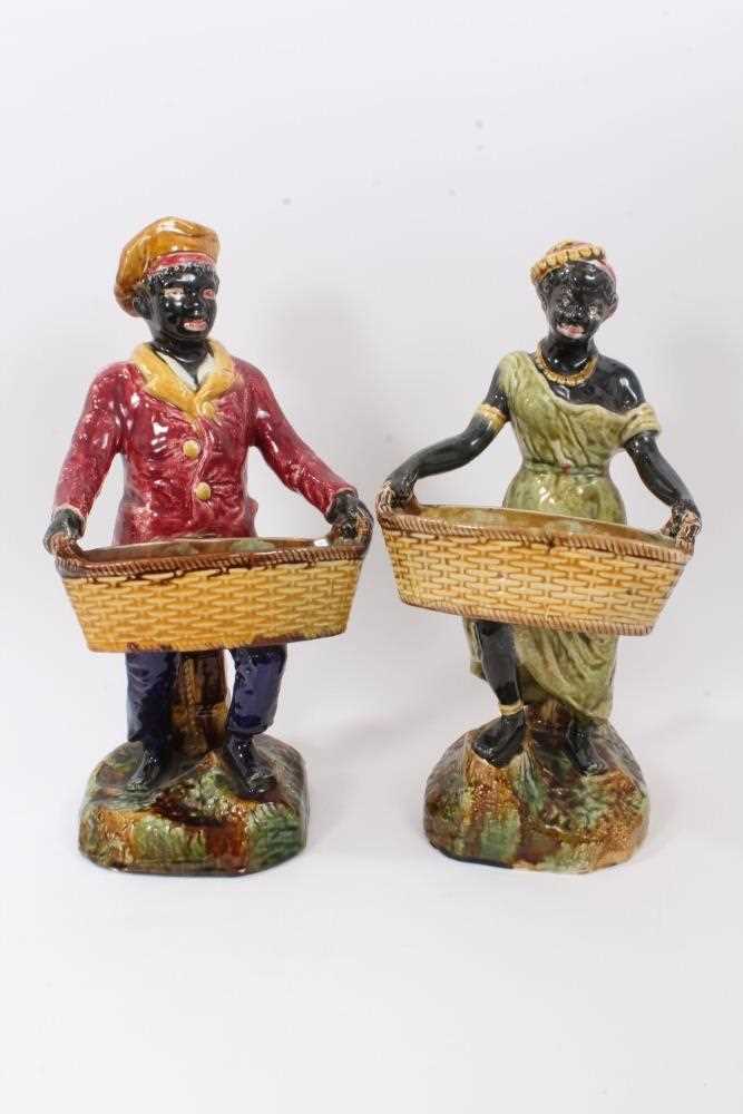 Lot 87 - Pair of continental majolica blackamoor figures, late 19th century, shown holding baskets and standing on grassy bases, 36cm and 38cm high