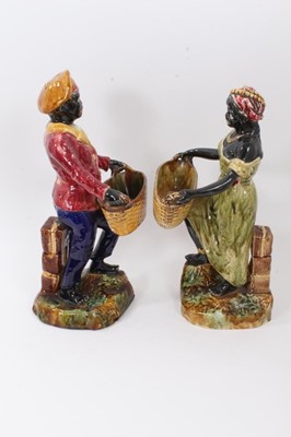 Lot 87 - Pair of continental majolica blackamoor figures, late 19th century, shown holding baskets and standing on grassy bases, 36cm and 38cm high