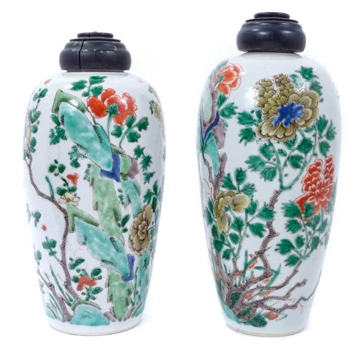 Lot 101 - A near pair of Chinese famille verte ovoid porcelain vases, Kangxi (1662-1722), decorated with flowers, birds and rockwork, with carved wooden covers, one with a double-ring mark to base, 23.5cm an...