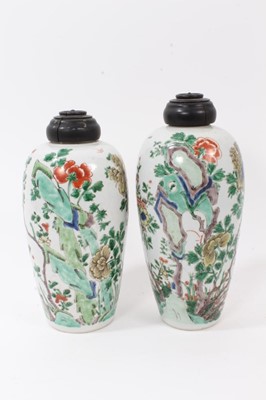 Lot 101 - A near pair of Chinese famille verte ovoid porcelain vases, Kangxi (1662-1722), decorated with flowers, birds and rockwork, with carved wooden covers, one with a double-ring mark to base, 23.5cm an...