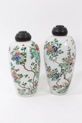 Lot 101 - A near pair of Chinese famille verte ovoid porcelain vases, Kangxi (1662-1722), decorated with flowers, birds and rockwork, with carved wooden covers, one with a double-ring mark to base, 23.5cm an...