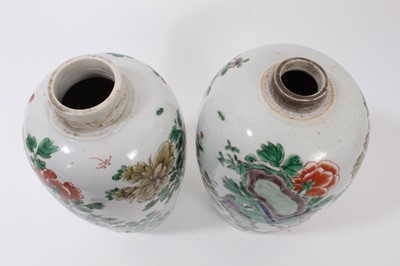 Lot 101 - A near pair of Chinese famille verte ovoid porcelain vases, Kangxi (1662-1722), decorated with flowers, birds and rockwork, with carved wooden covers, one with a double-ring mark to base, 23.5cm an...