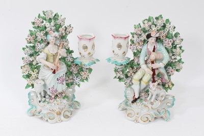 Lot 195 - Pair of Derby figural candlesticks, circa 1770, modelled as musicians, with a dog and sheep by their sides, seated within floral encrusted bocage, on gilt and blue enamelled scrollwork bases, 19.5c...