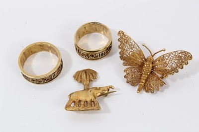 Lot 204 - Two Middle Eastern yellow metal rings, yellow metal elephant palm tree brooch and yellow metal filigree butterfly brooch (4)