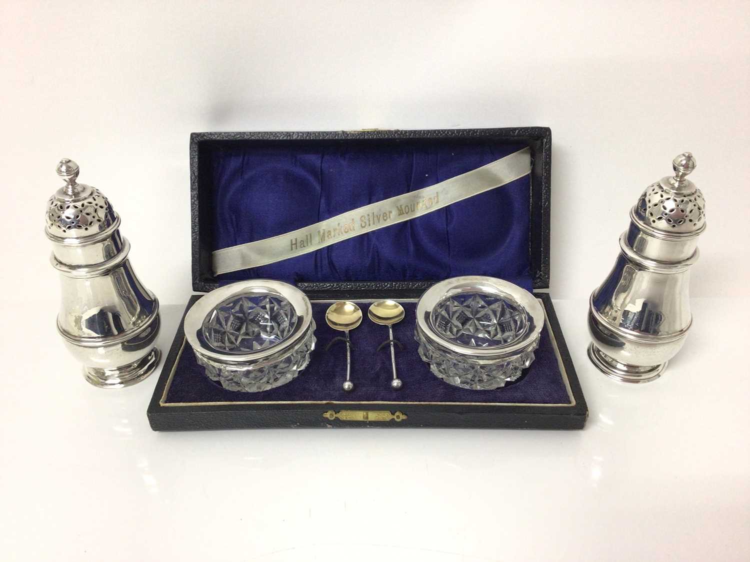 Lot 124 - George V silver salt and pepper, of baluster form, with reeded decoration and pierced tops, hallmarked for London 1915, together with a pair of cased silver-mounted cut glass salts with silver spoo...